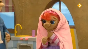 Een foto van de pop Sassa in de keuken met een doek om haar hoofd en schouders.