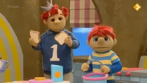 Een foto van de poppen Koning Koos en Toto in de keuken. Toto heeft een winkelmandje in de hand en Koning Koos wat brood.