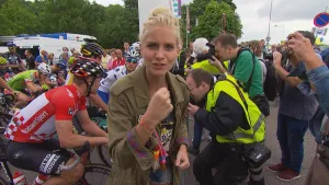 Foto van presentator die staat voor wielrenners en fotografen, de wielrennen zijn aan het einde van een rit gekomen.