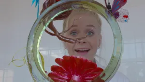 Foto van presentator, je ziet alleen haar hoofd, die kijkt door een groot doorzichtig suikerkunstwerk.