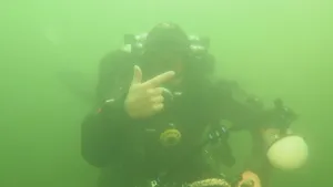 Foto van een duiker onderwater met een onderwatertoestel, maakt ermee ergens een foto van.