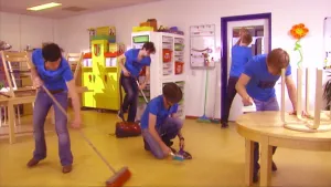 Foto van groep mensen in het blauw gekleed die een schoolklas schoonmaken.