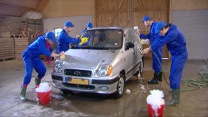 Foto van aantal mannen in blauwe werkkleding die een auto in de garage aan het wassen zijn.