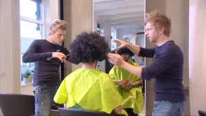 Foto van man die bij de kapper zit en twee kappers, mannen, zijn met zijn haar bezig.