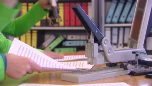 foto van een grote perforator op tafel en je ziet de armen van iemand die iets doet met grote vellen papier.