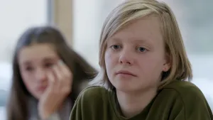 Foto van een somber kijkend meisje, portret, ernaast ander meisje minder scherp in beeld.