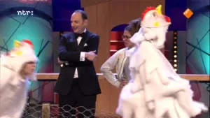 Foto van de presentator van Snugger in de studio, voor hem lopen twee personen verkleed als een witte kip.