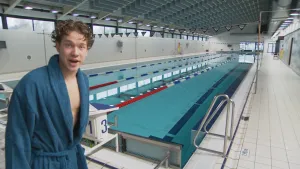 Foto van presentator die staat bij een lang diep indoor wedstrijdzwembad.