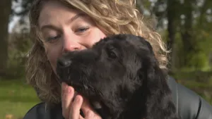Foto van een vrouw, je ziet haar hoofd, vlakbij een zwarte hond, je ziet de kop ervan.