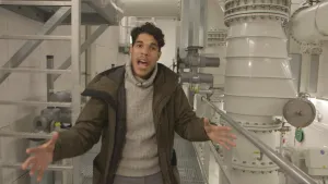 Foto van presentator die staat in een vertrek met machines van een rioolwaterzuivering.