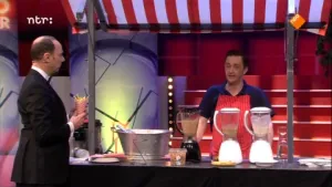 Foto van de studio van Snugger waarin de presentator staat bij een marktkraampje waarin een man staat bij keukenapparatuur.