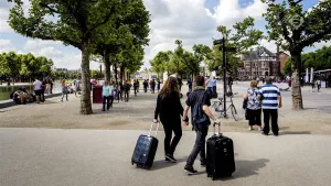 Foto van een plein in een stad met veel mensen en twee toeristen met bagage die er lopen.