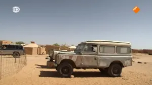 Foto van een woonwijkje in Bachir in Wonderland, met woestijn waarop een grote jeep/landrover staat.