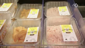 Foto van aantal plastic bakjes met kip erin in schap van de supermarkt.