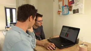 Foto van een jongen en een man die samen aan tafel bezig zijn aan de laptop.
