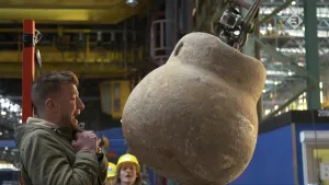 Foto van presentator in grote fabriekshal met een enorm grote sloopkogel.