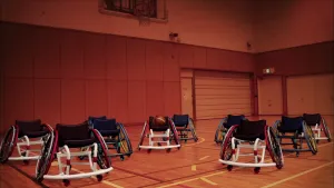 Foto van sportzaal waarin dansende rolstoelen zonder mensen erin basketbal spelen.
