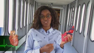 Foto van presentator in smalle gang in een gebouw die het model van een hart vasthoudt.
