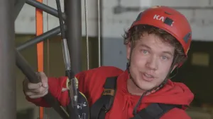 Foto van een industrieel klimmer met werkkleding en klimtuig aan, helm op.