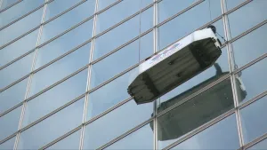 Foto van een glazenwassersbakje dat hoog hangt aan flat met ramen, erin ramenwassers.