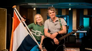 Foto van Ilse de Lange samen met presentator, Ilse houdt een Nedelandse vlag met wimpel vast.