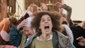 Foto van vrouw die schreeuwt/roept, je ziet haar gezicht, erachter aantal mannen die hun handen opsteken.