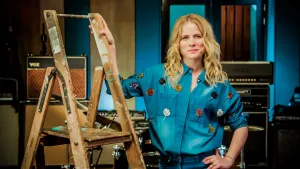 Foto van Ilse de Lange die staat bij een houten trappetje in een ruimte met muziekboxen.