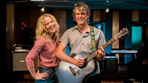 Foto van Ilse de Lange die staat bij een man die speelt op een gitaar.