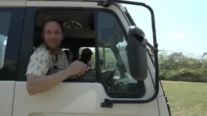 Foto van man die zit voorin een grote witte auto , hij rijdt mee door de natuur.