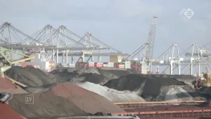 Foto van een industriehaven met op de voorgrond opslag met grote bergen zand, kolen etc.