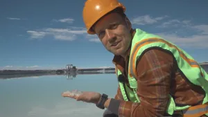 Foto van een man in werkkleding met helm op die staat bij een groot water en heeft iets wits (zout?) op zijn hand liggen.