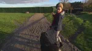 Foto van presentator die met een hond loopt over een pad door een groot grasveld heen.