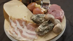 Foto van een plankje met aantal soorten kaas, ham en nog wat producten erop, producten met een umami smaak.