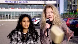 Foto van presentator die buiten voor een middelbare school staat en een jong meisje interviewt.