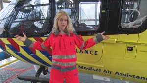 Foto van presentator in felle werkkleding die staat voor een traumahelikopter.