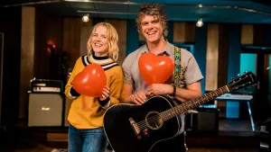 Foto van Ilse de Lange en Ronnie Flex die elk een hartvormige rode ballon vasthouden en Ronnie ook een gitaar.