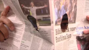 Foto van een opengeslagen krant door iemand vastgehouden met twee kijkgaten erin.