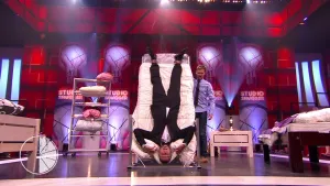 Foto van de studio van Snugger waarbij een aangeklede man ondersteboven ligt in een rechtopstaand bed.