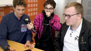 foto van presentator die een man interviewt met microfoon, er staat nog een man bij.