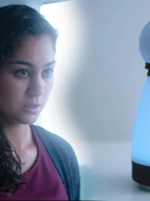 Foto van presentator, portret, die staat bij een soort plastic witte pop, lijkend op een bowlingpin, Rita.