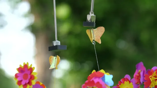 Foto van twee magneten waaraan draden met vlindertjes van papier hangen.
