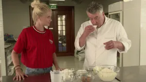 Foto van presentator en een man die voor aantal kommen met ingrediënten voor te koken staan.