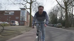 Foto van presentator die fietst over een rustige straat in een stad.