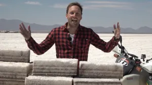 Foto van presentator die staat bij een witte vlakte, een zoutwoestijn te Bolivia, voor hem liggen grote blokken zout.