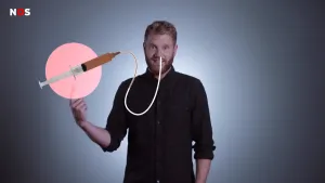 Foto van presentator die staat met eroverheen getekend alsof hij een grote injectiespuit met poep erin via een slangetje in zijn mond spuit.