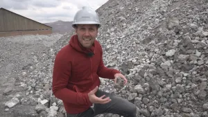Foto van presentator die zit aan de rand van grote berg zilvererts in een zilvermijn.