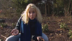 Foto van presentator die op haar hurken zit op de grond in een bos met bladeren erop.