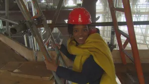 Foto van presentator met helm op in een zaal in de Domtoren te Utrecht, tussen steigers die daar staan.