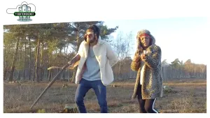 Foto van een verklede man en vrouw, de man houdt een jachtgeweer vast, die lopen door de natuur.