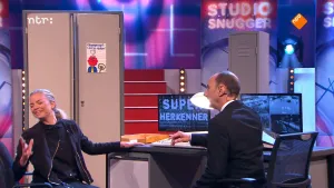 Foto van de presentator van Snugger die aan tafel zit, vrouw zit erbij, in de studio.